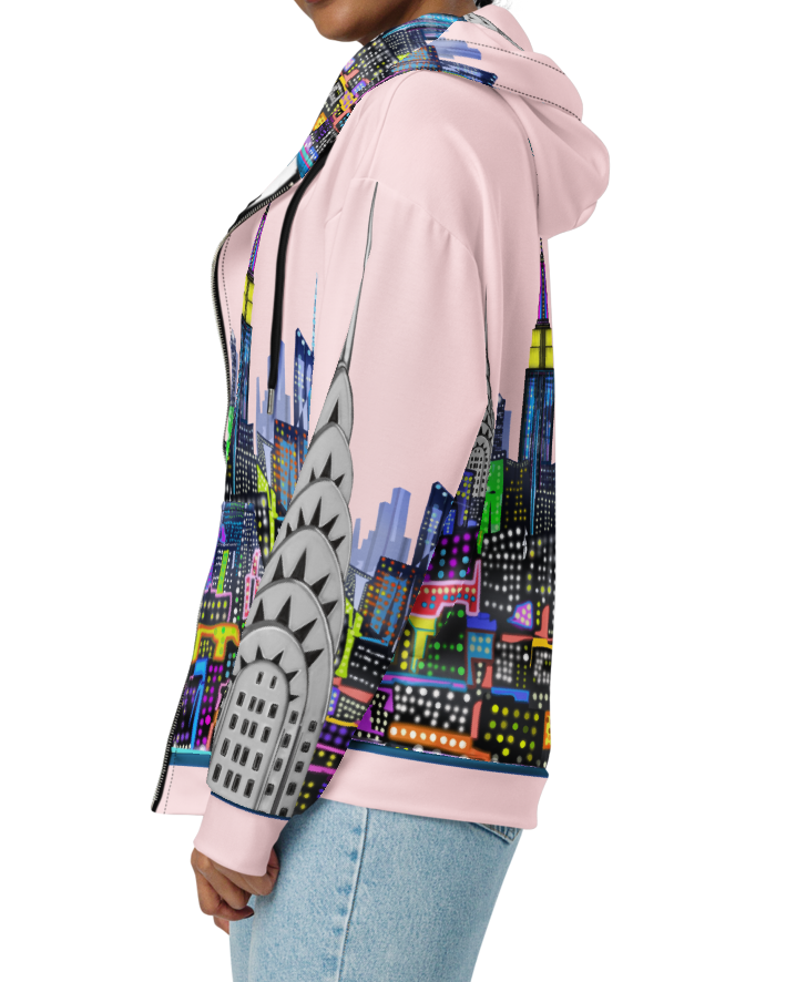 Woman wearing a colorful Loria NYC Art hoodie with a cityscape design on a white background