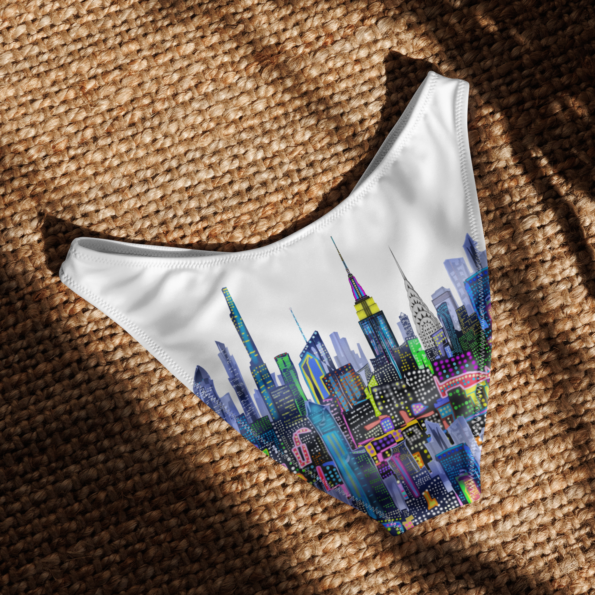 Colorful cityscape design on a white Loria NYC Art bikini bottom laid on a textured brown surface