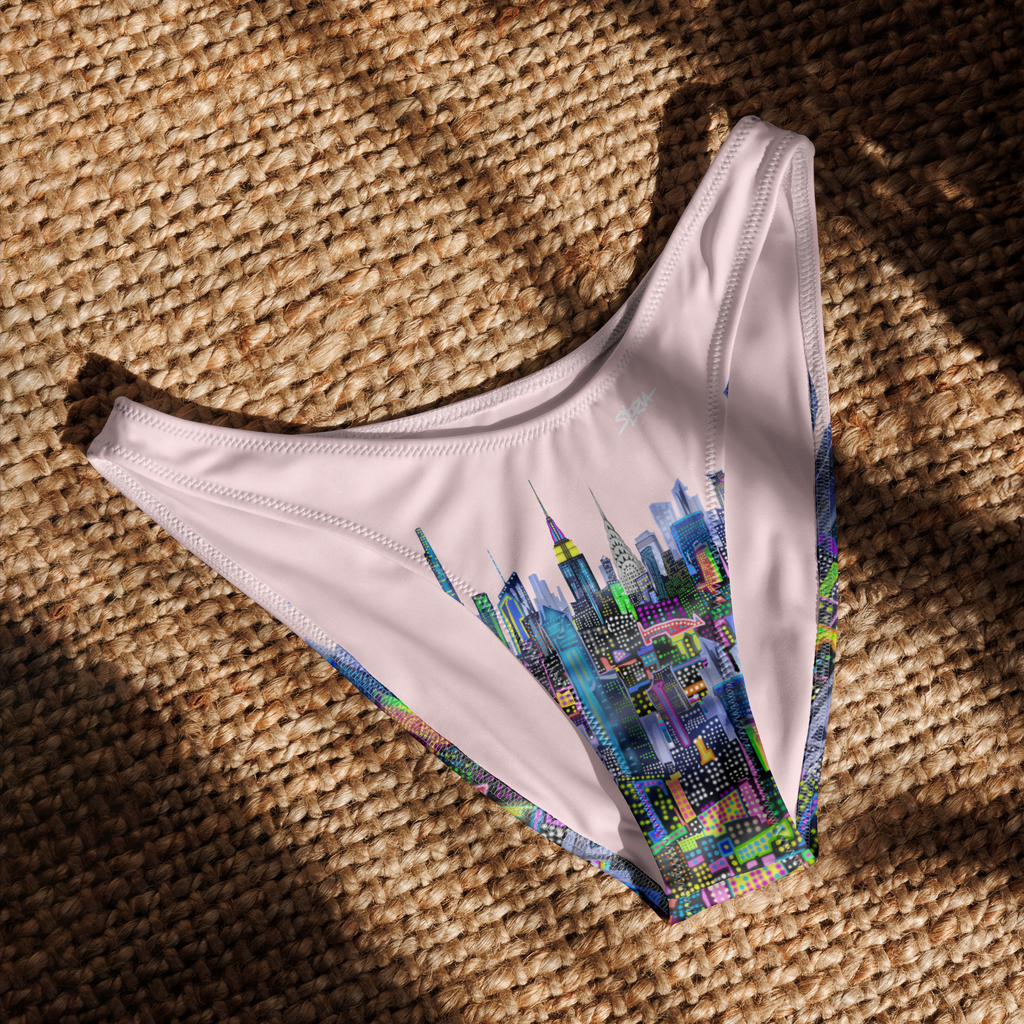 White bikini bottom with colorful Loria NYC Art cityscape design on a textured brown surface