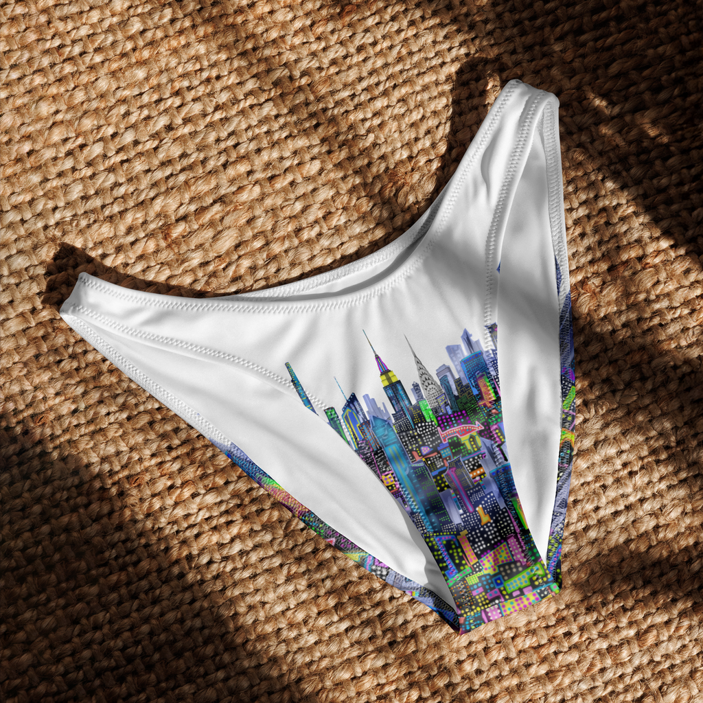 White bikini bottom with colorful cityscape Loria NYC Art design on a textured brown surface