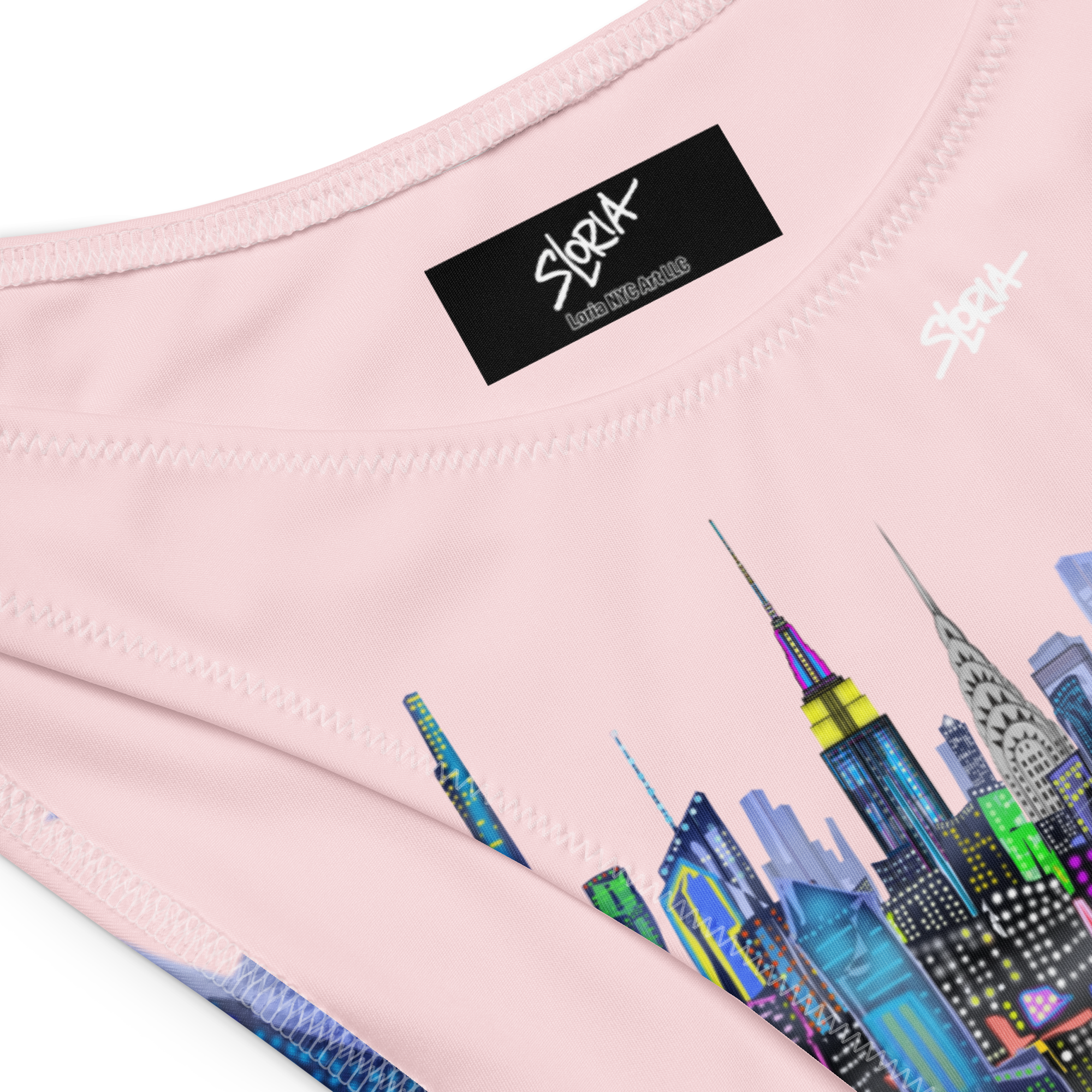 Close-up of a pink garment with a Loria NYC Art colorful cityscape design and a brand label.