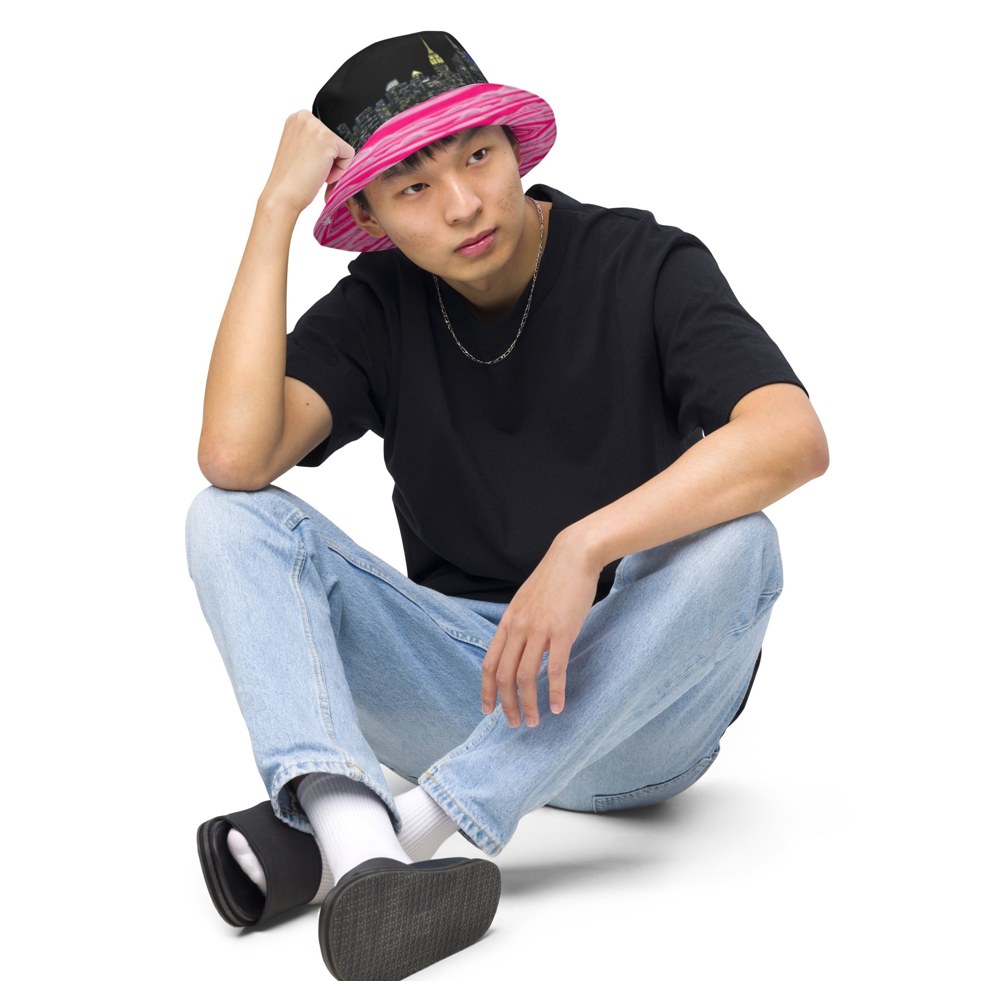 Man sitting down wearing  Reversible Bucket Hat with Città Rosa Vento Fuchsia NYC skyline designed with Brooklyn bridge by S.Loria NYC