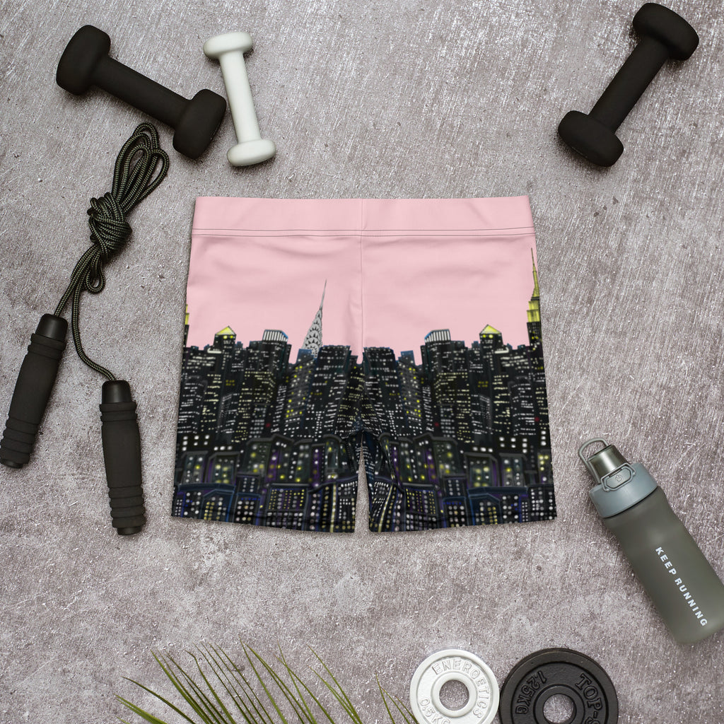 Pink athletic shorts with  Loria NYC Art skyline design on a gray surface with fitness equipment.
