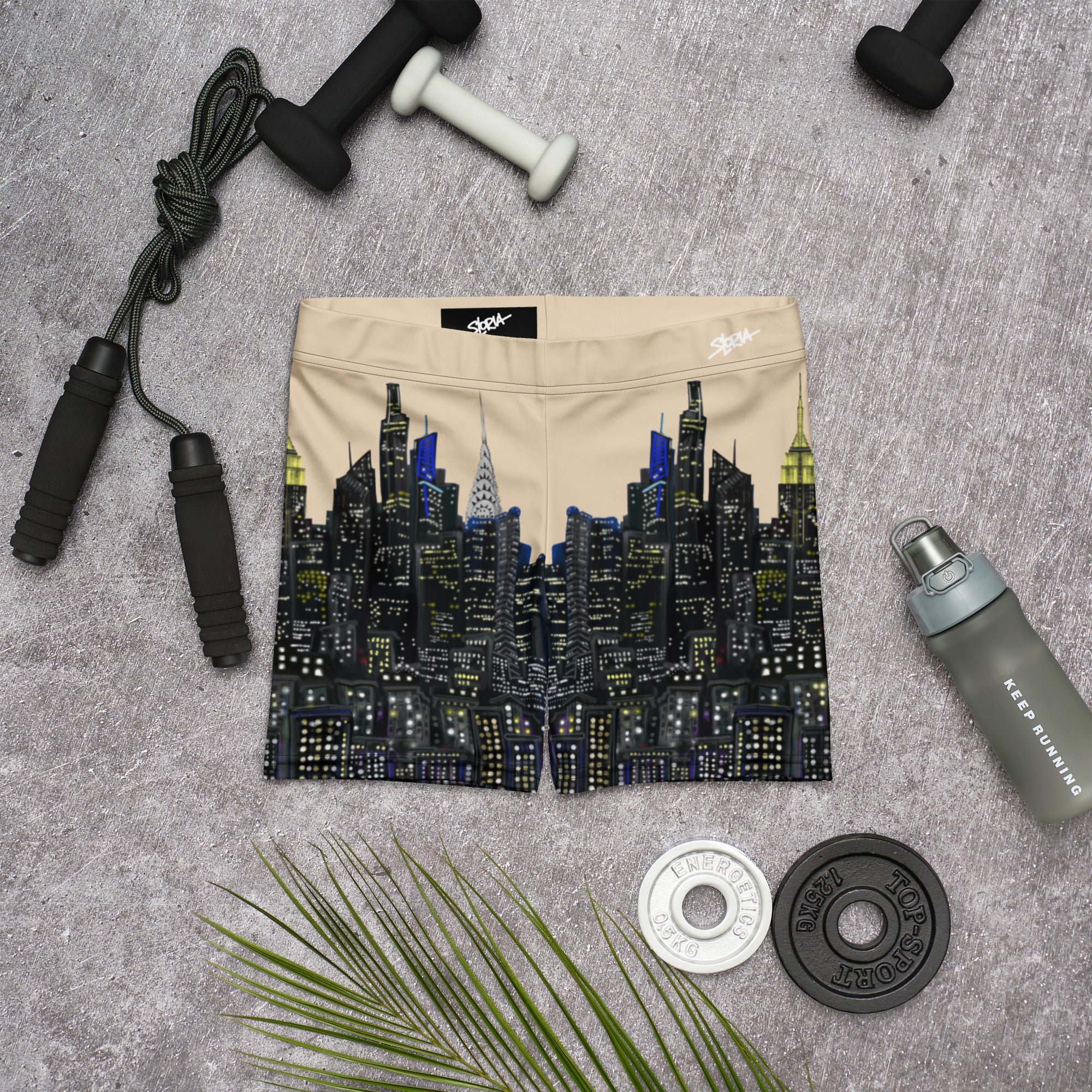 Beige shorts with cityscape design on a gray surface with fitness equipment.