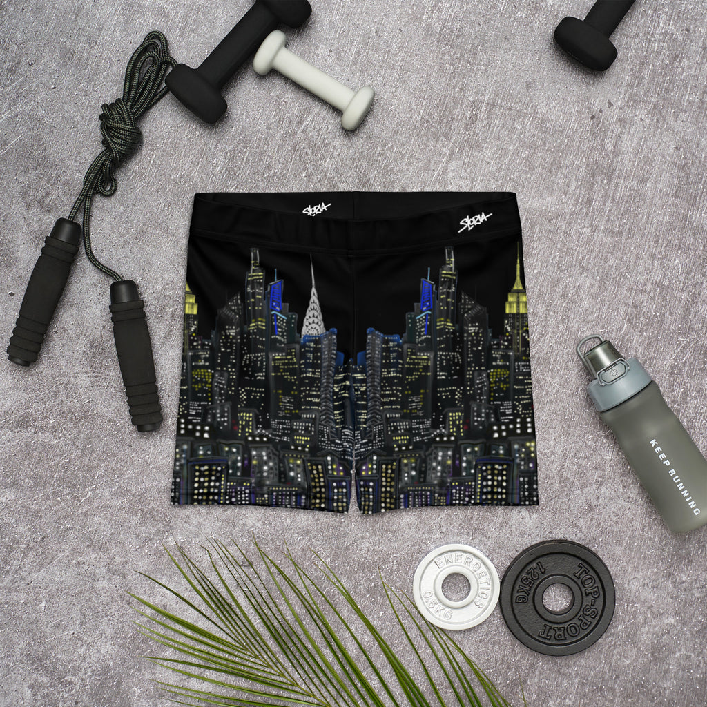Black swim shorts with cityscape Loria NYC Art design on a gray surface with fitness equipment.