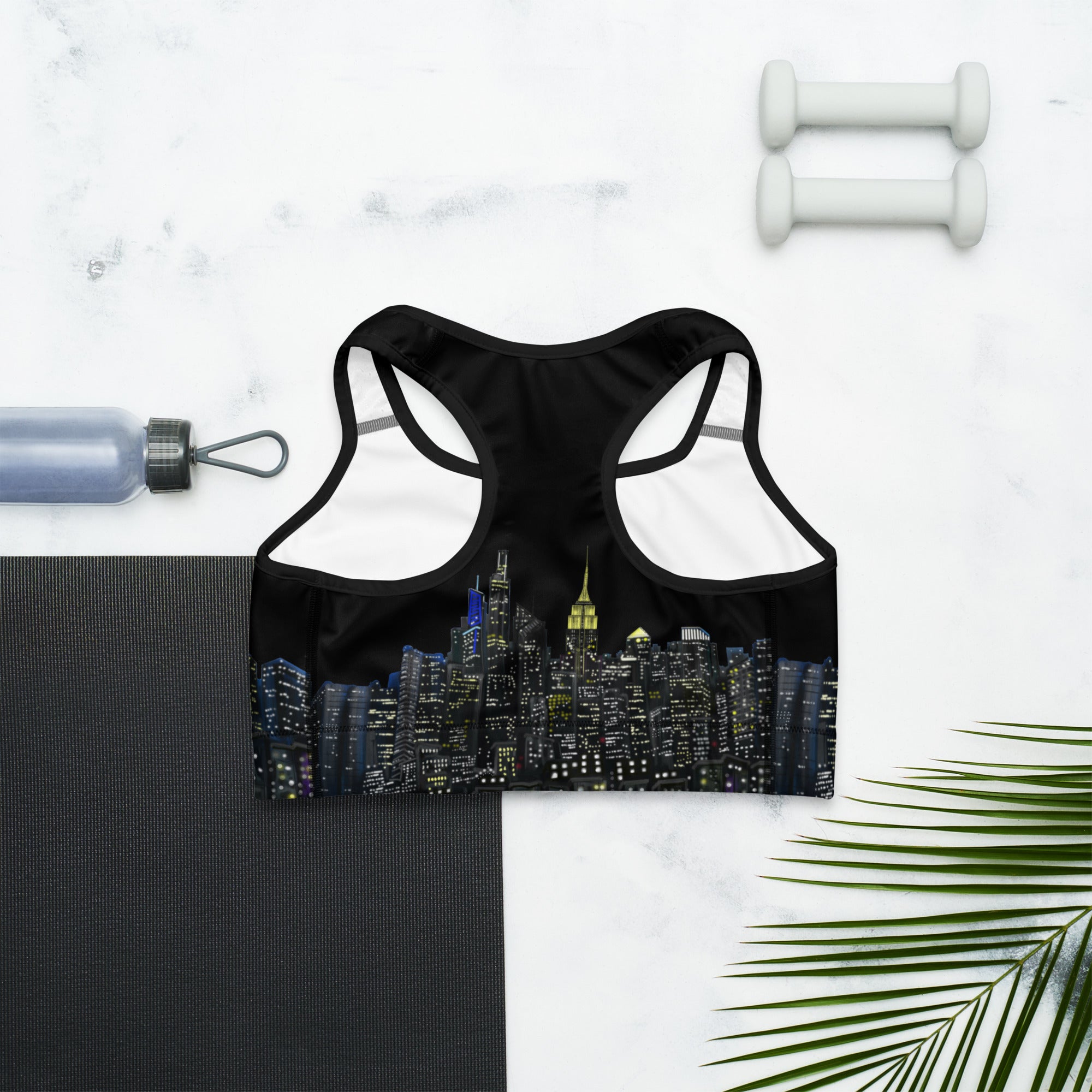 Back of Black sports bra with cityscape design on a white marble surface with fitness items.