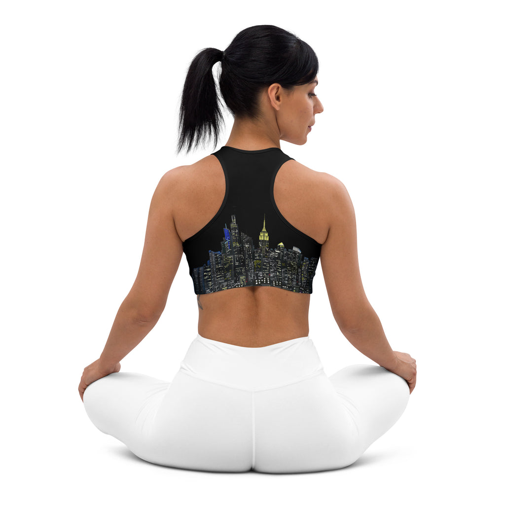 Woman wearing a black sports bra designed by Loria NYC Art with cityscape design and white leggings in yoga a position on a white background