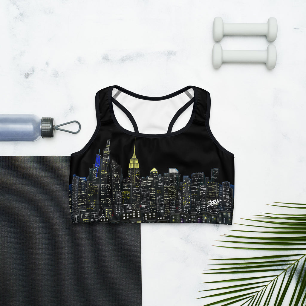 Black sports bra with cityscape design on a marble surface with a yoga mat, water bottle, and dumbbells.