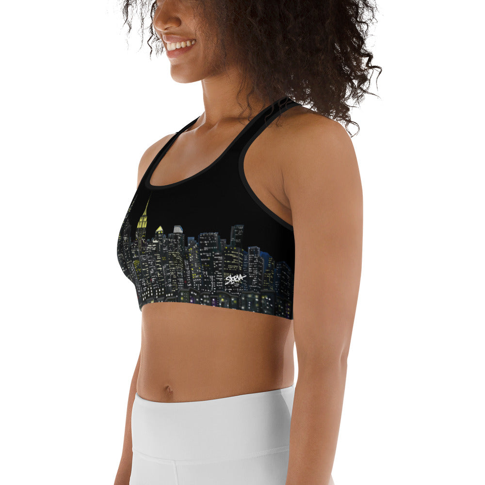 Woman wearing a black sports bra designed by Loria NYC Art with cityscape design and white leggings on a white background