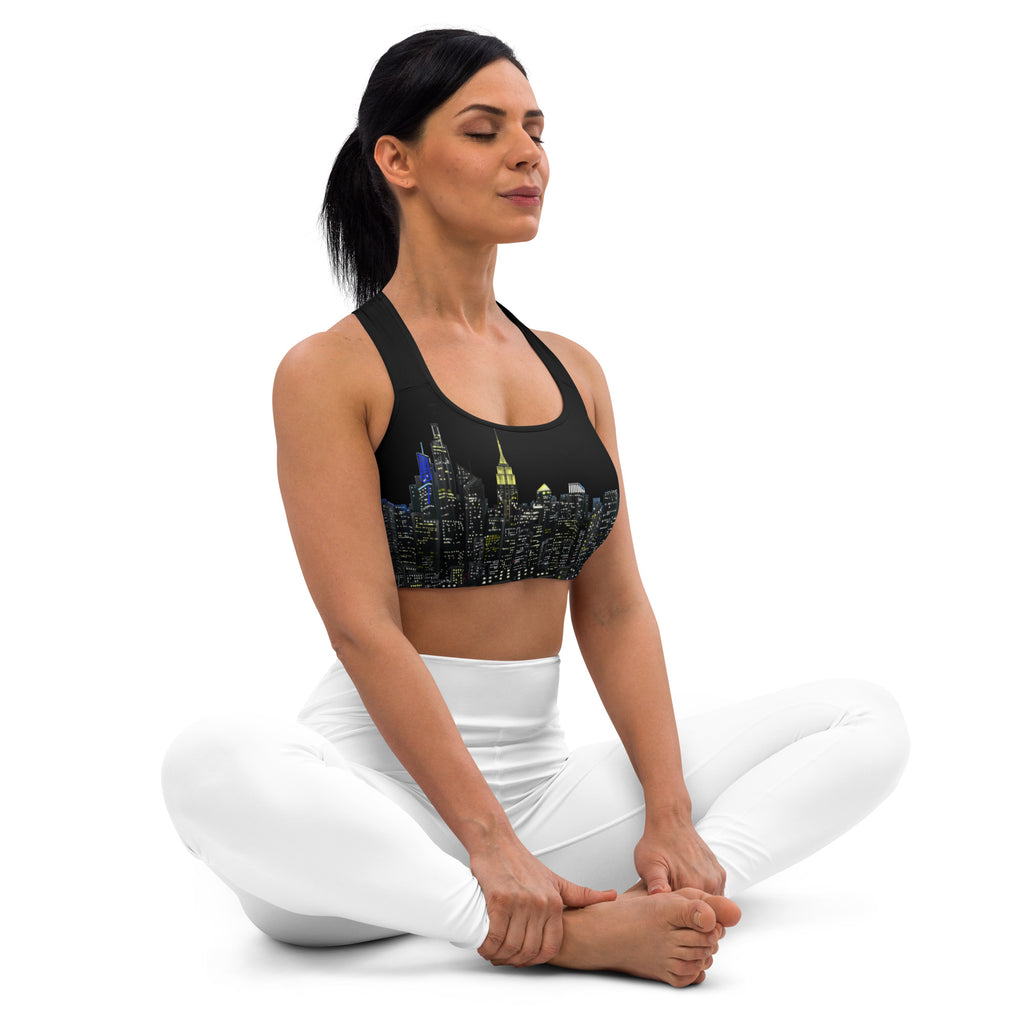 Woman wearing a black sports bra designed by Loria NYC Art with cityscape design and white leggings in yoga a position on a white background