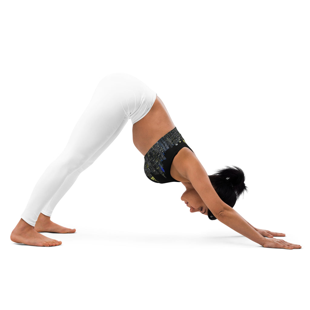 Woman wearing a black sports bra designed by Loria NYC Art with cityscape design and white leggings in yoga a position on a white background
