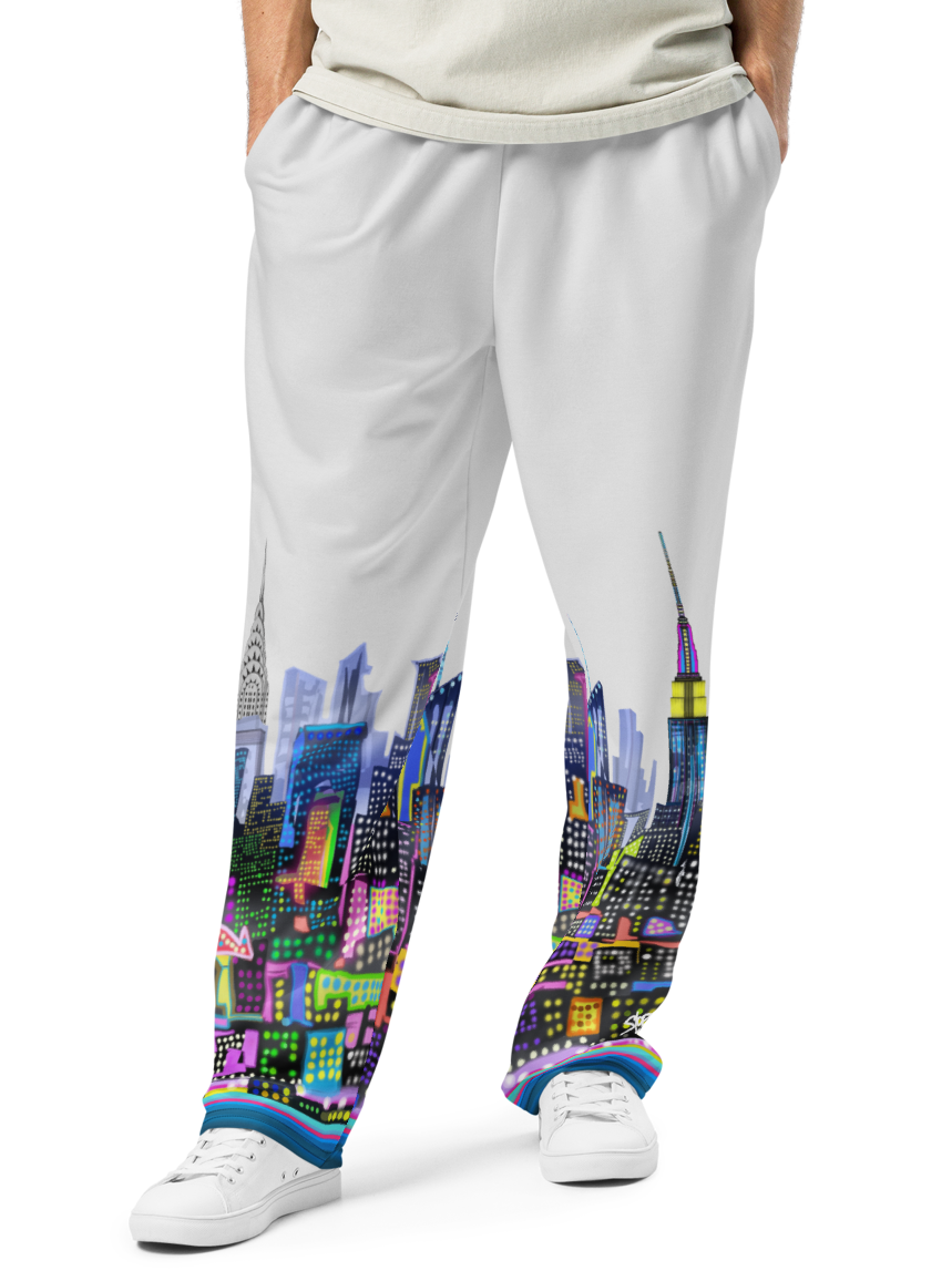 Person wearing a light gray t-shirt and white pants with a colorful Loria NYC Art cityscape design on a white background