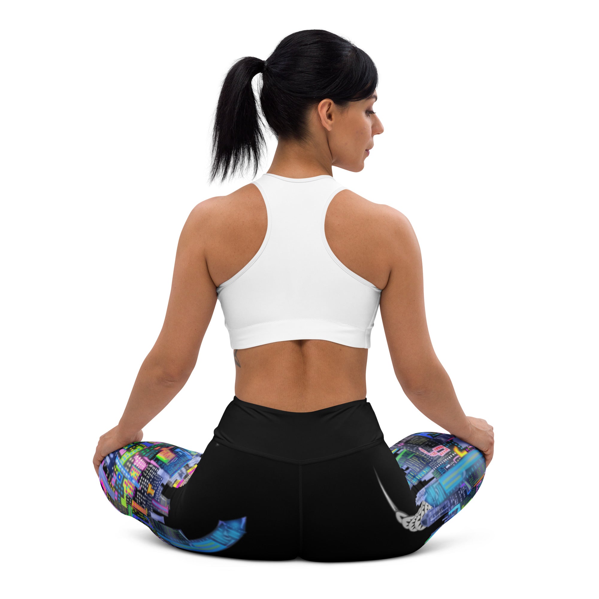 Person sitting in a yoga pose wearing colorful Loria NYC Art leggings and a white sports bra, on a white background