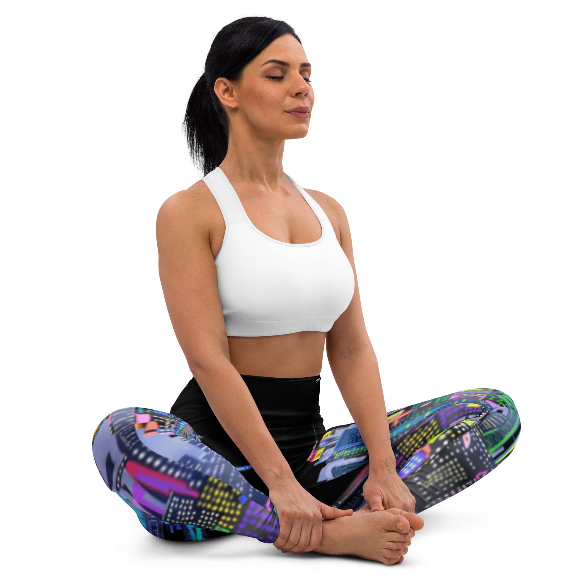 Woman sitting in a yoga pose wearing colorful  Loria NYC Art leggings and a white sports bra on a white background