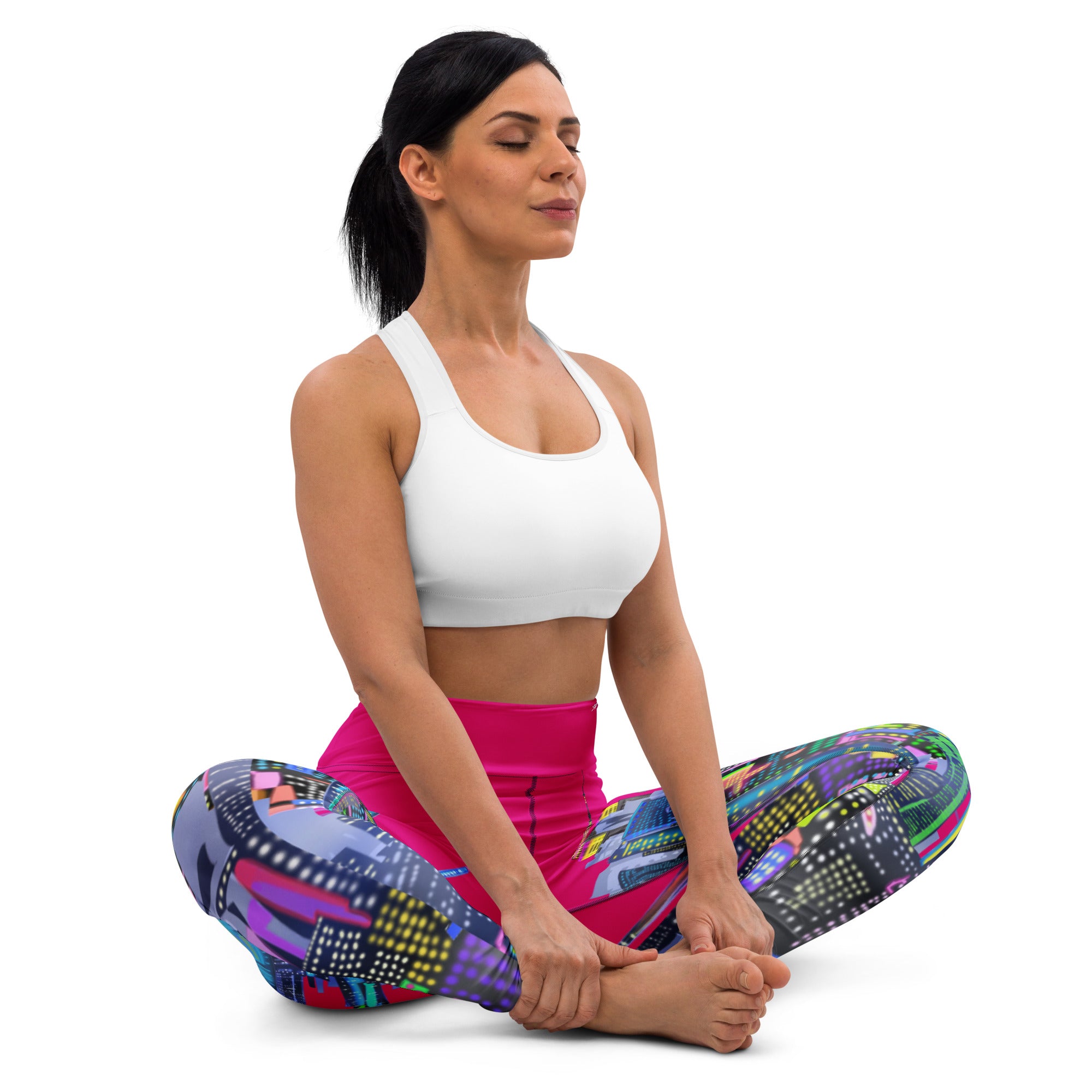 Woman sitting in a yoga pose wearing colorful Loria NYC Art pants and a white top on a white background