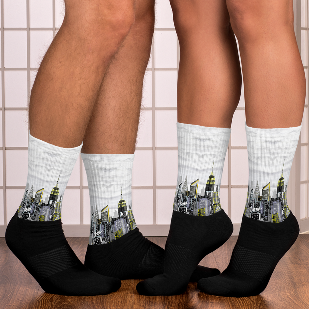 Two pairs of socks with Loria NYC Art  cityscape design on a tiled floor background