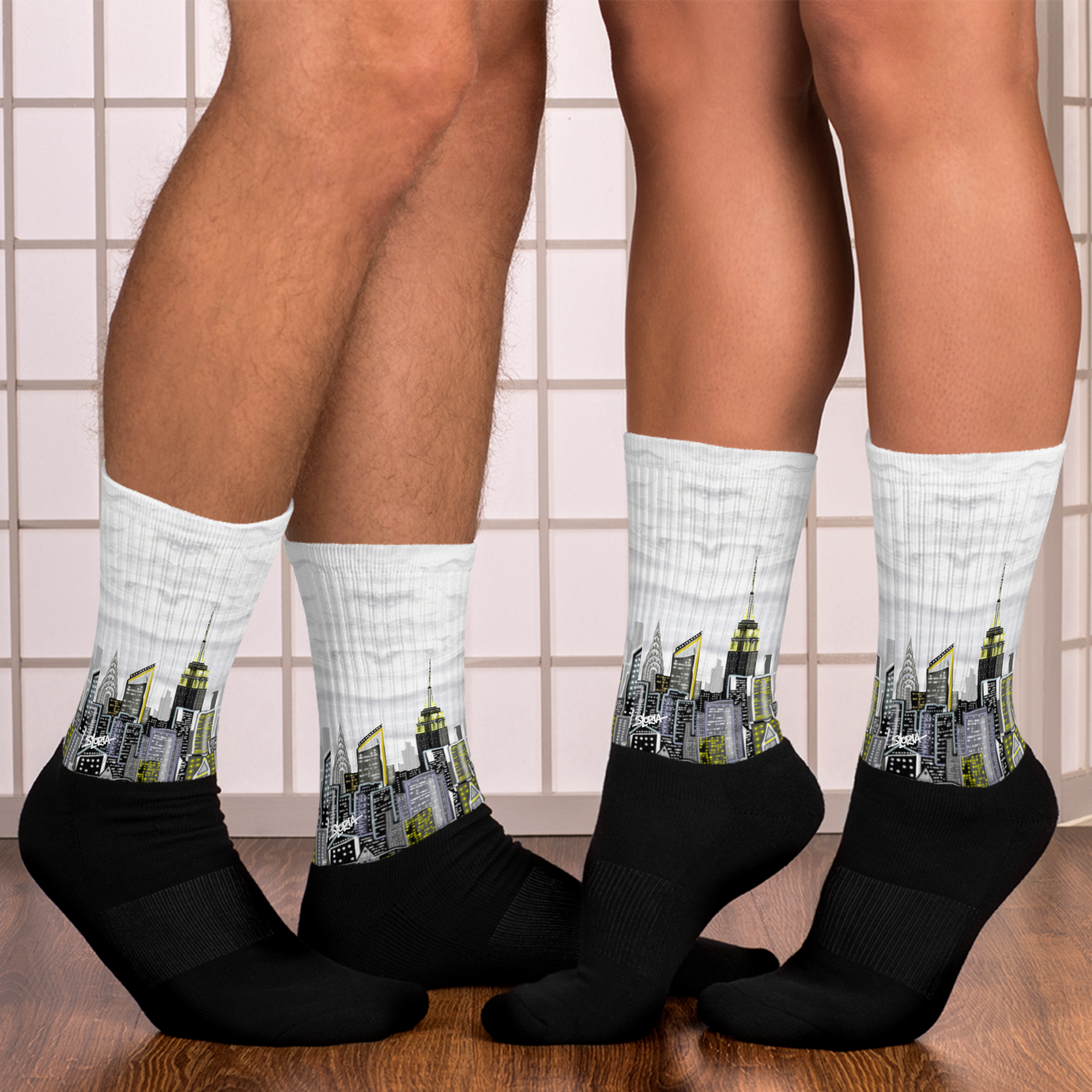 Two pairs of socks with Loria NYC Art  cityscape design on a tiled floor background