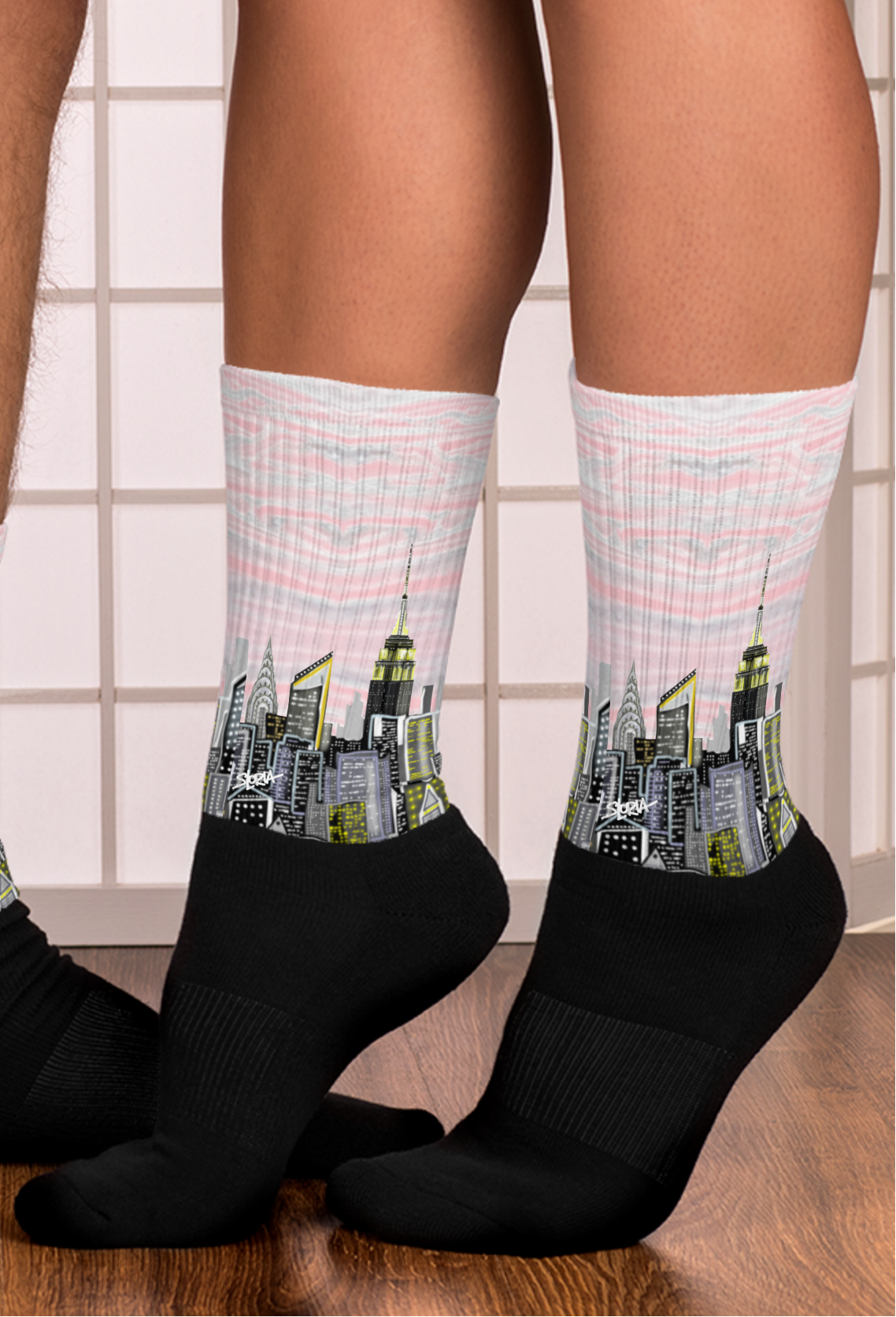 Loria NYC Art Cityscape socks with black socks worn indoors on a wooden floor.