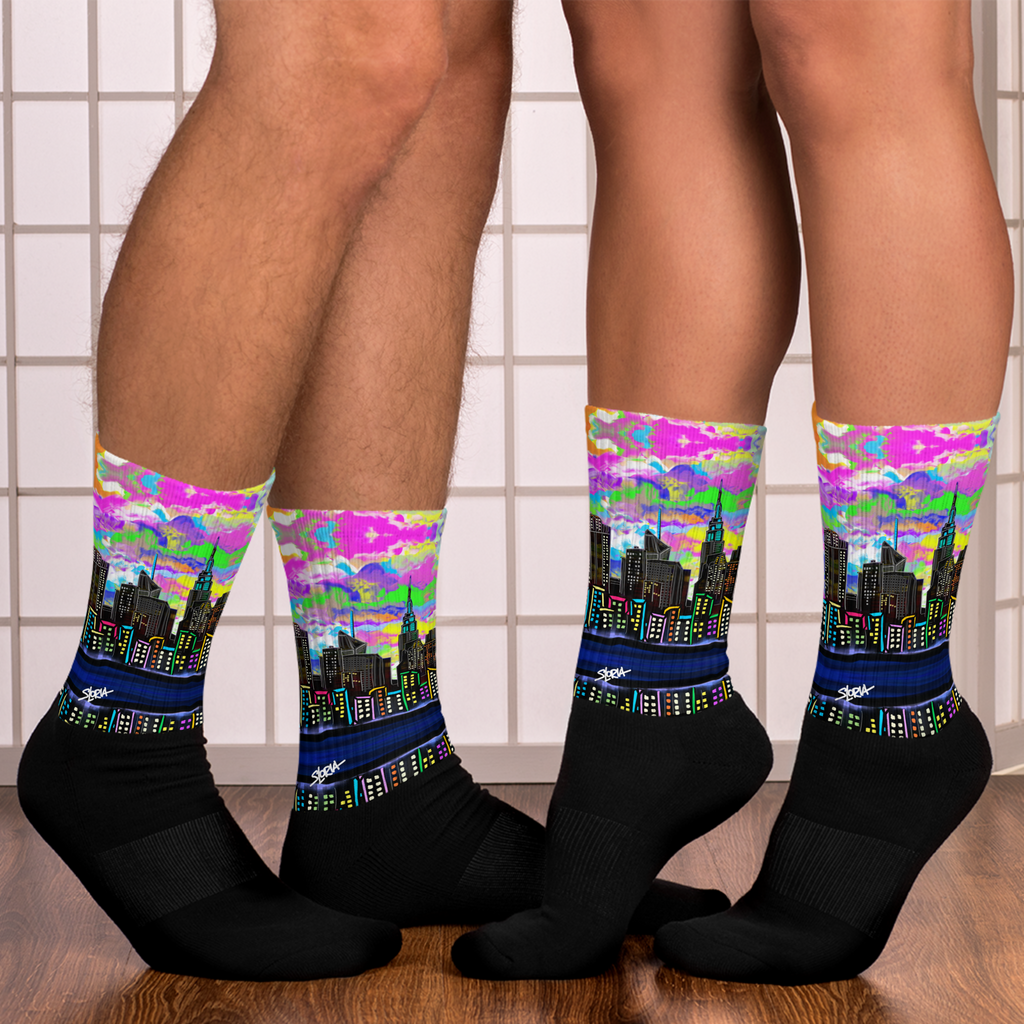 Colorful cityscape Loria NYC Art socks worn by a person on a tiled bathroom floor.