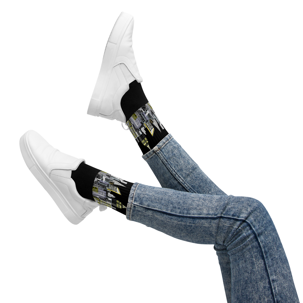 Legs wearing blue jeans, white sneakers, and black Loria NYC Art socks with a futuristic design on a white background