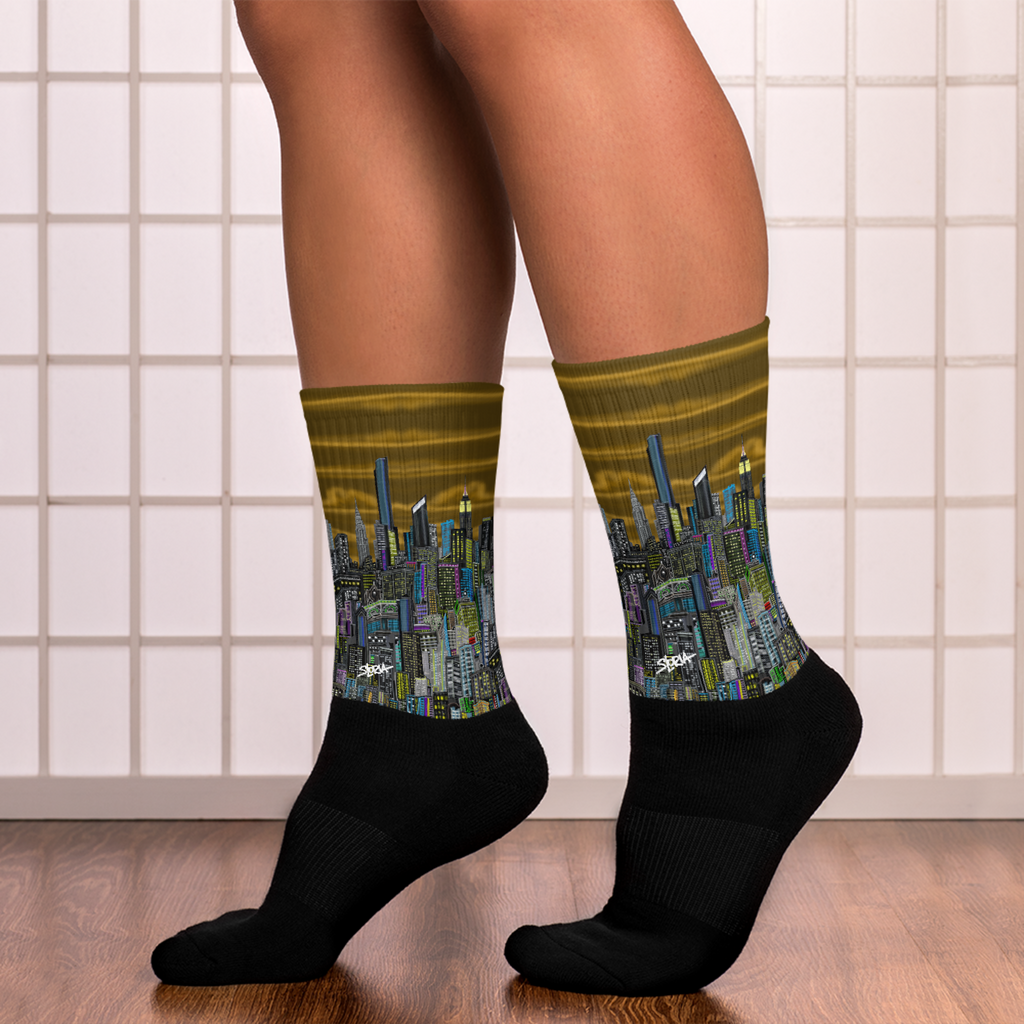 Black socks with cityscape Loria NYC Art design worn by a person on a tiled floor.