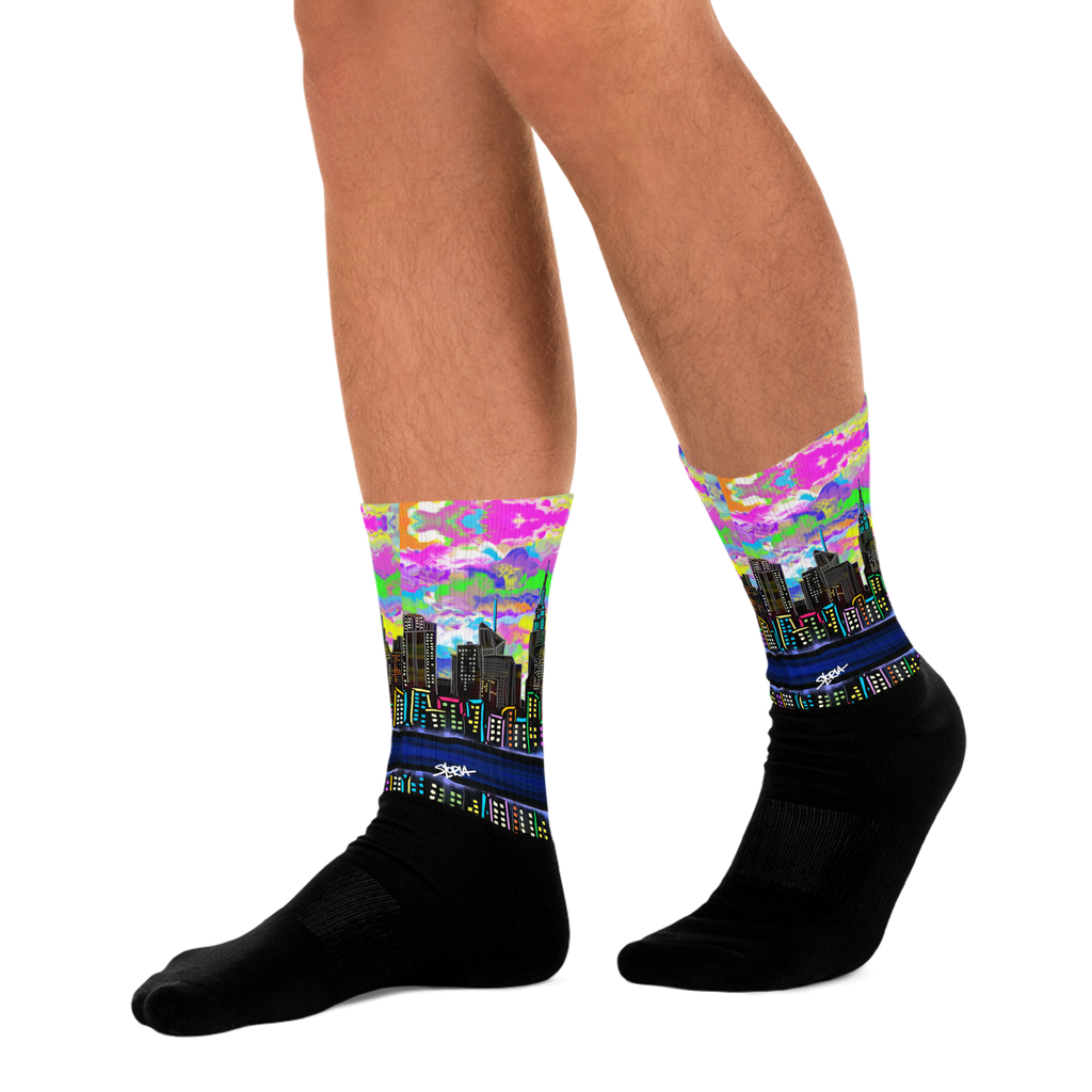 Colorful cityscape Loria NYC Art socks with black soles worn by a person on a white background