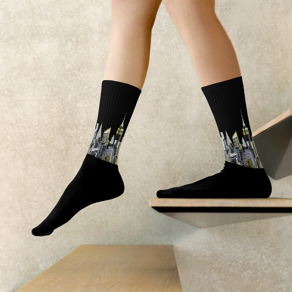 Black socks with cityscape Loria NYC Art design worn by a person on a light wooden floor.