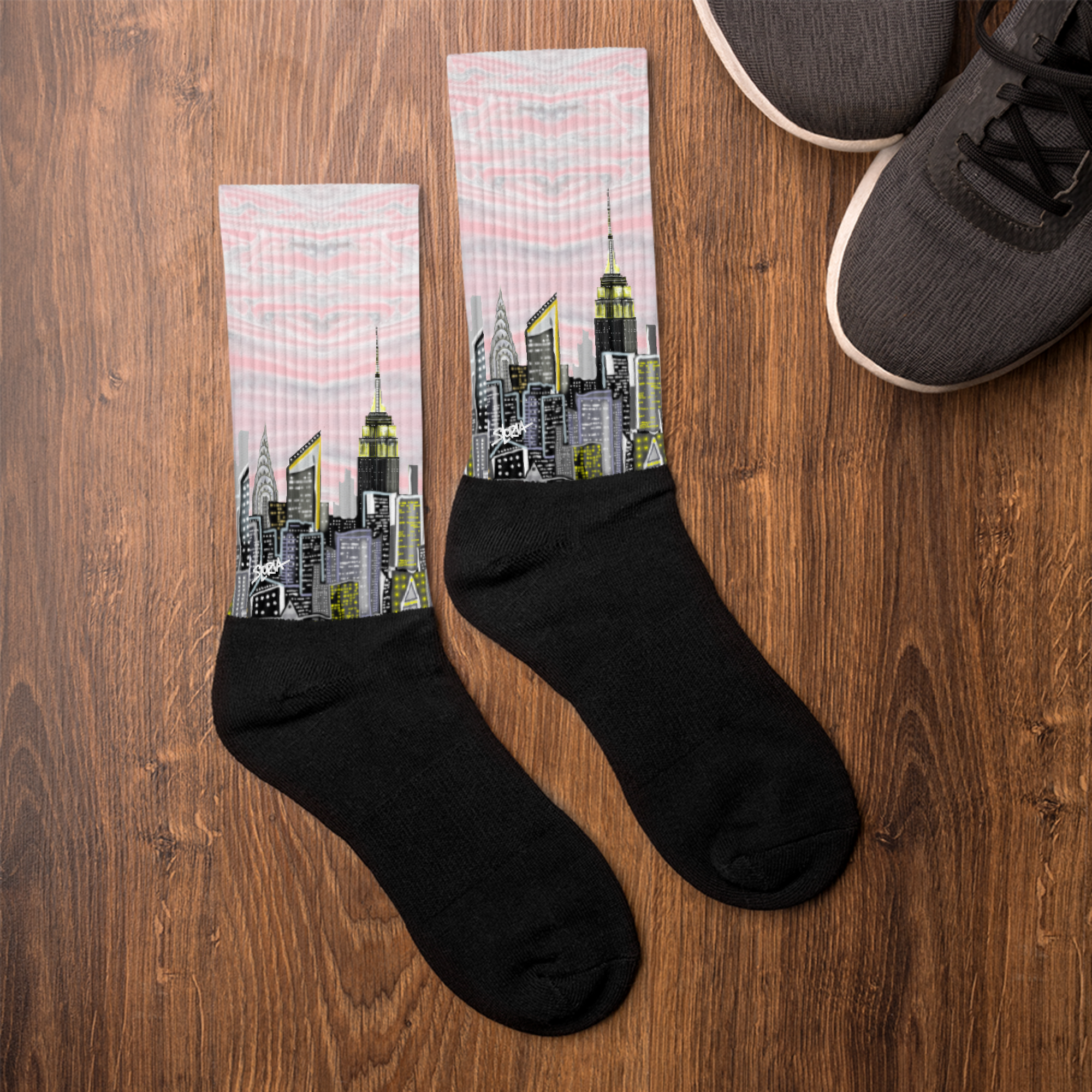 Loria NYC Art socks with cityscape design on a wooden surface next to a pair of shoes.