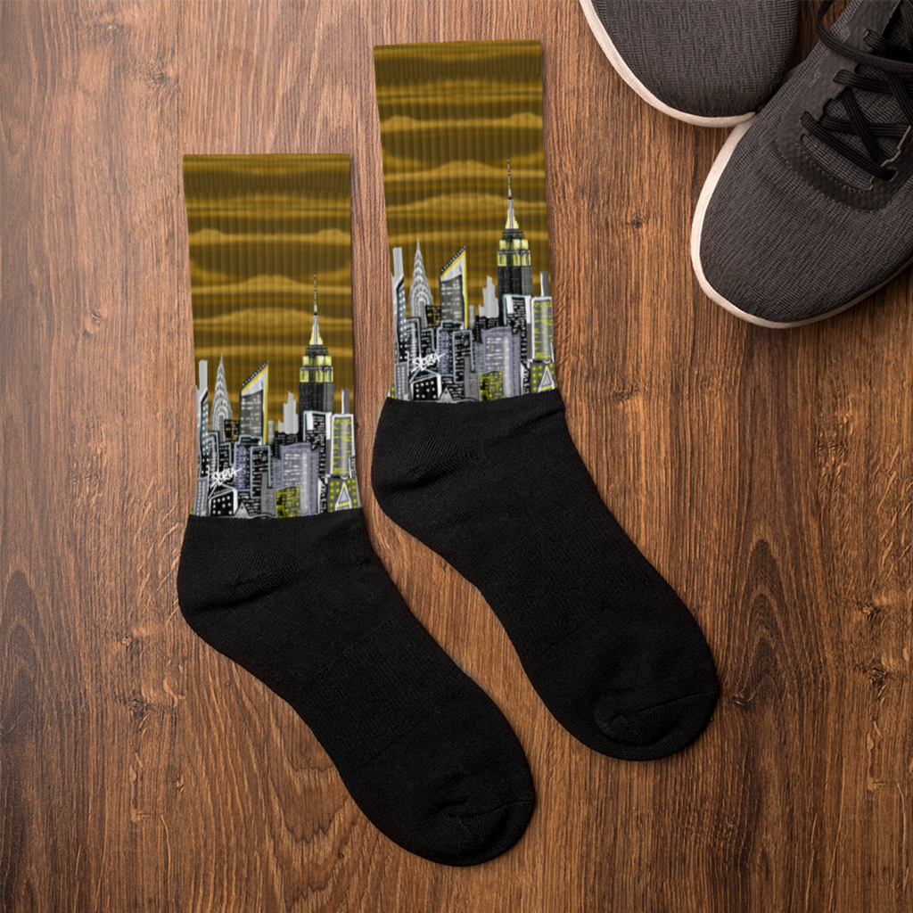 Black socks with cityscape Loria NYC Art design on a wooden surface next to a shoe