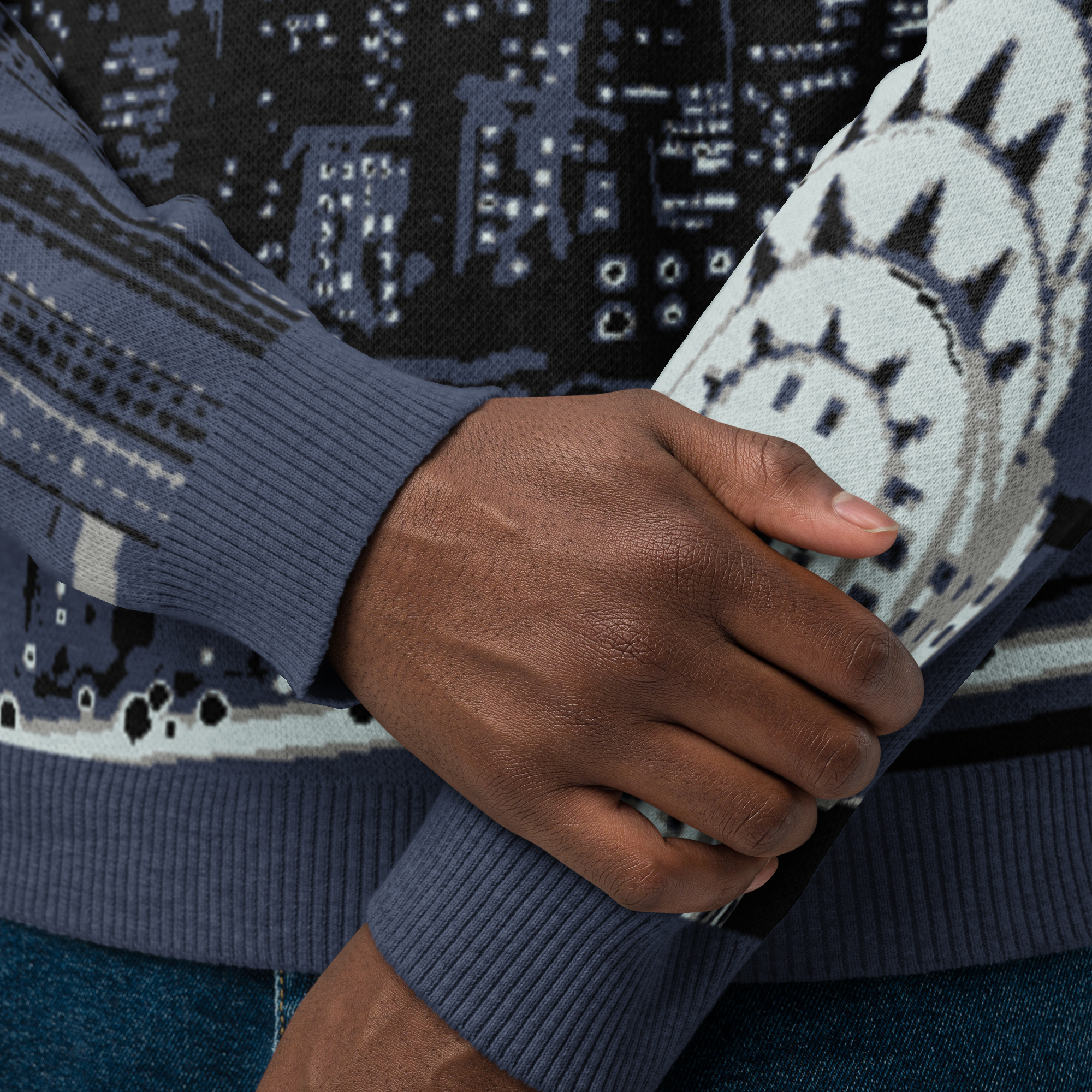 Close-up of a person wearing a dark blue sweater with a Loria NYC Art cityscape pattern, holding their arm.