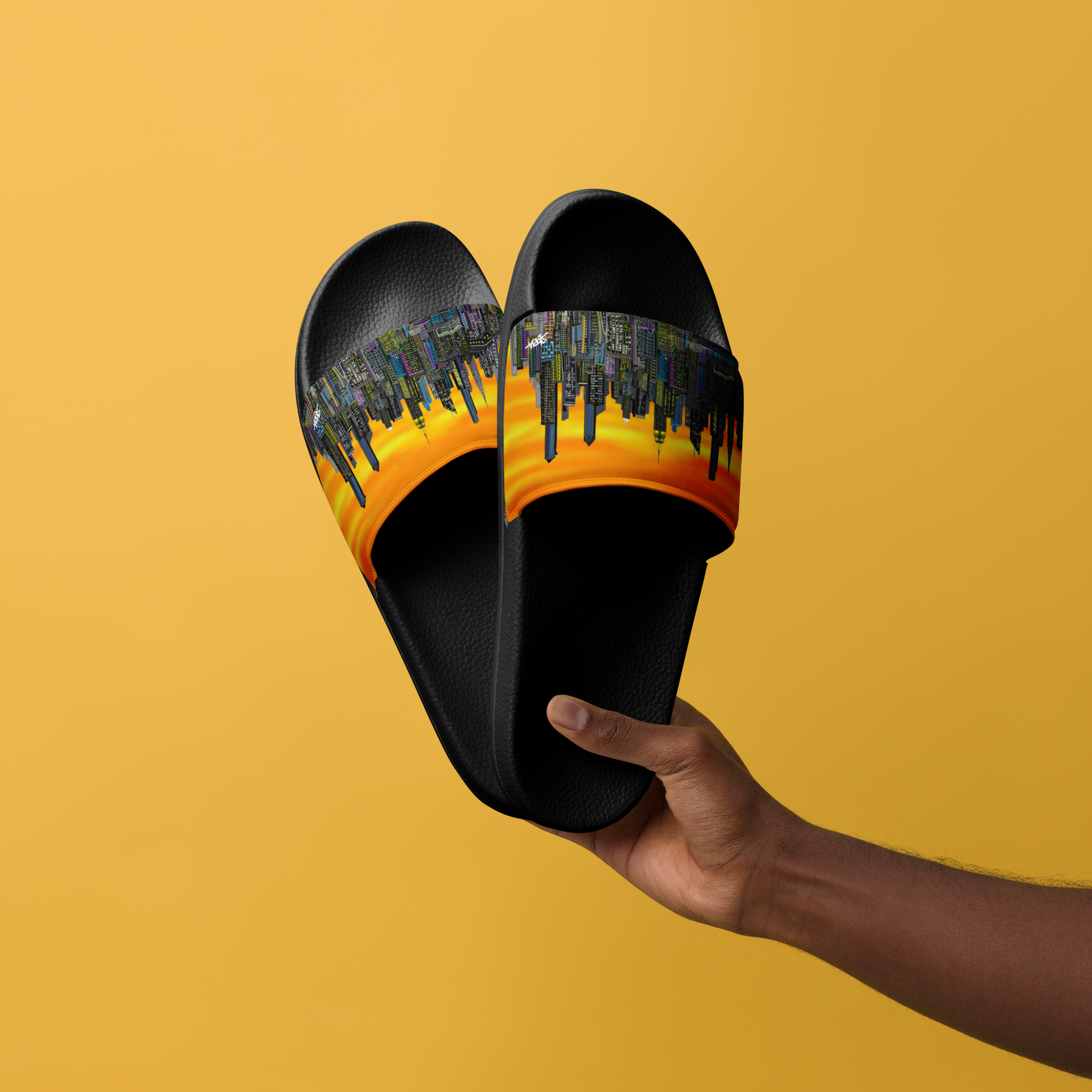 Black slide Loria NYC Art sandals with a cityscape design held by a hand against a yellow background