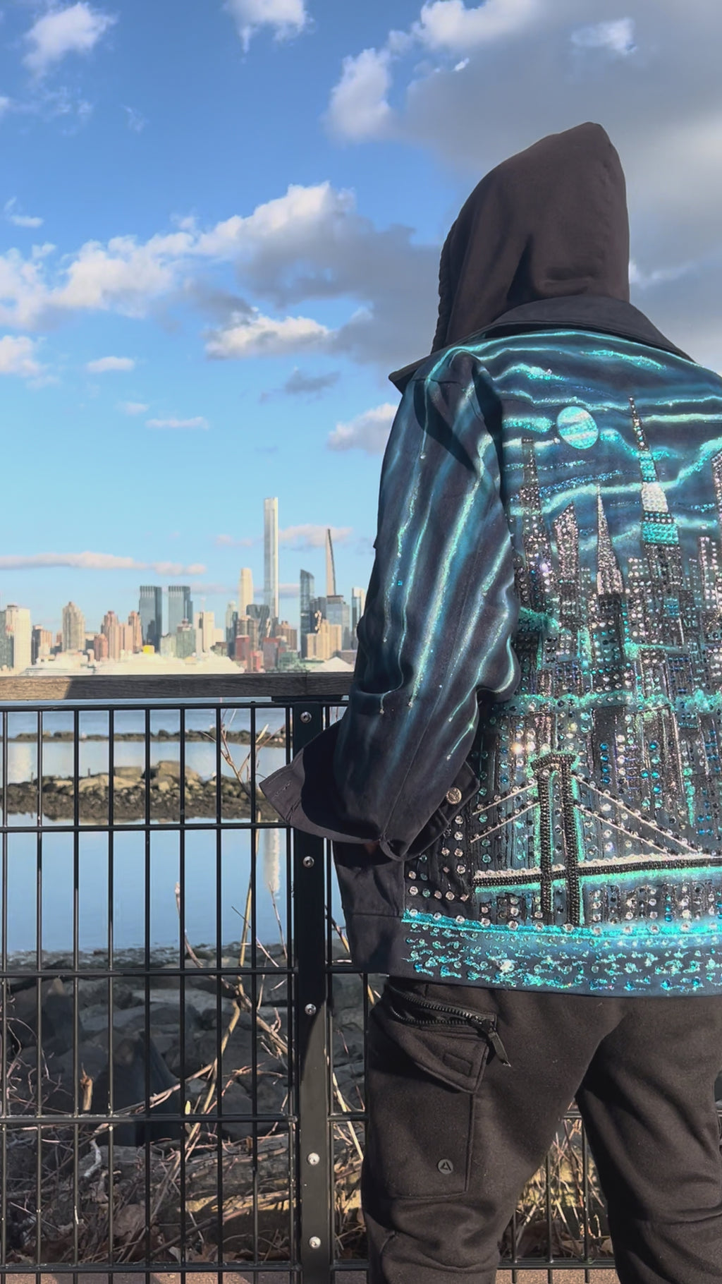 Close up vertical Video on a clear day of a man wearing a  jacket covered in Loria NYC Art with skyline background
