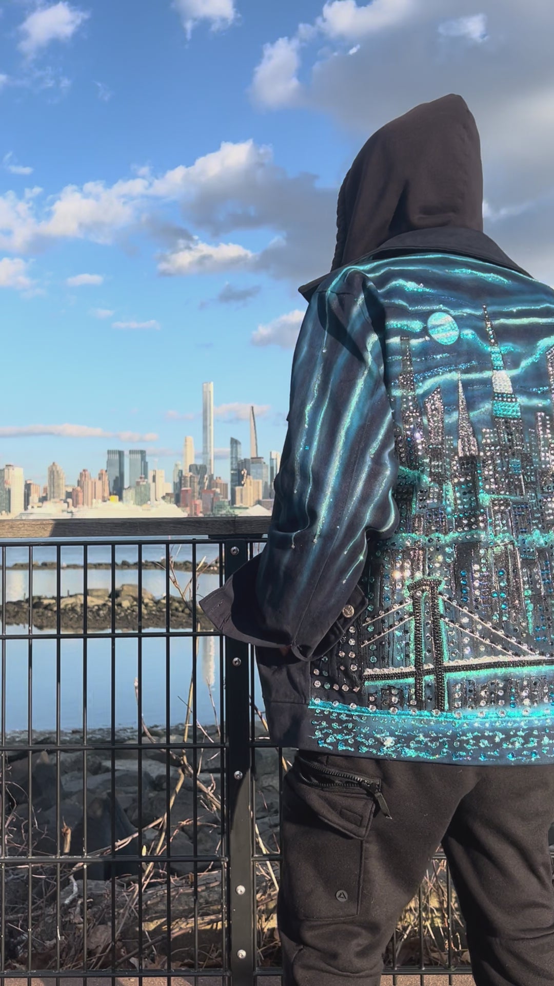 Close up vertical Video on a clear day of a man wearing a  jacket covered in Loria NYC Art with skyline background