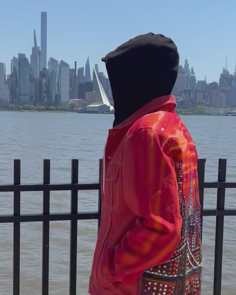 Person walking in a video wearing a vibrant orange Loria NYC Art jacket looking at  the city skyline in the background.