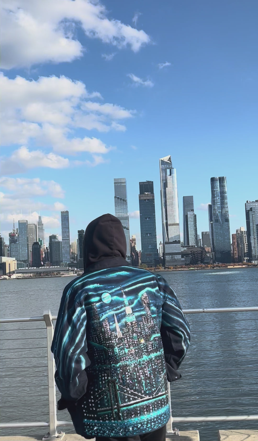 Video of man  on a clear day wearing a  jacket covered blue colorful Loria NYC Art with skyline background