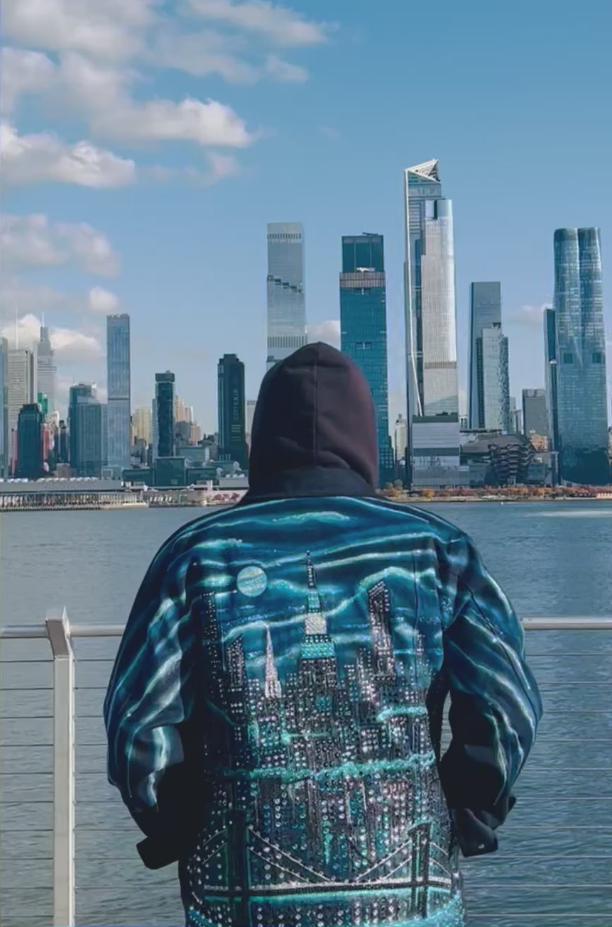 Man wearing a reflective blue colorful Loria NYC Art jacket with the skyline in the background.