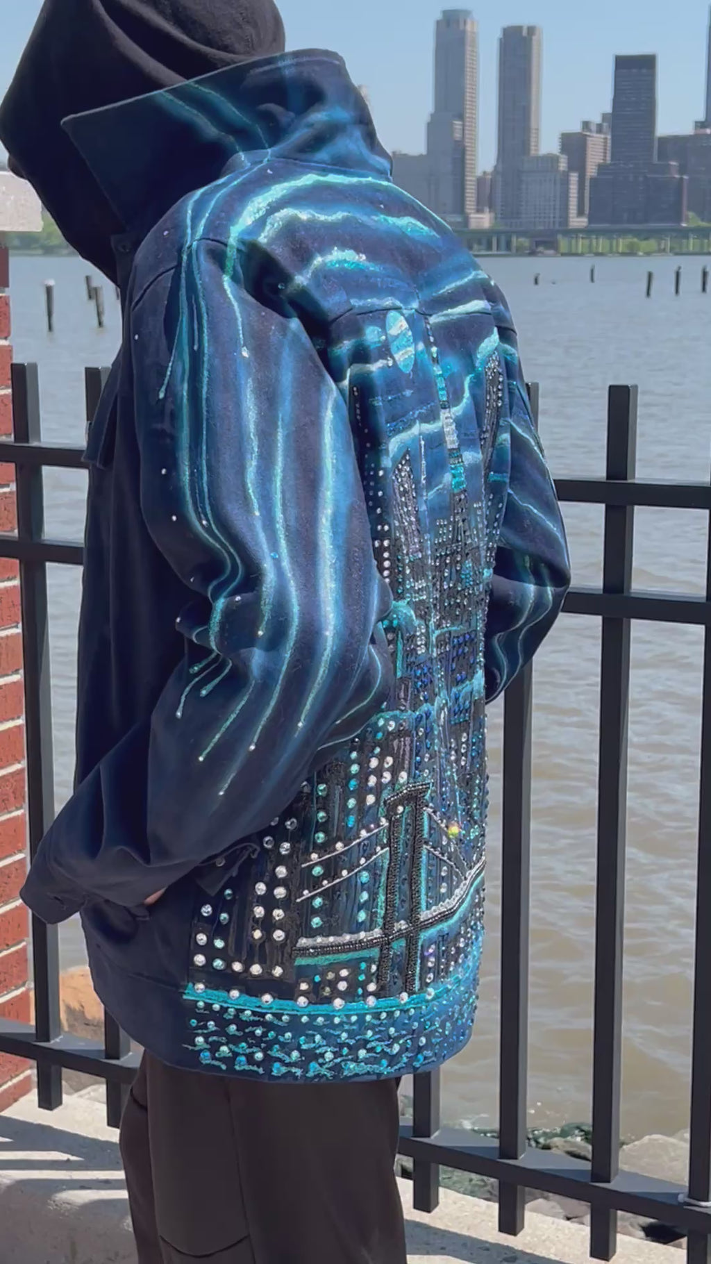Blue jacket with Loria NYC Art on the back with the city skyline in the background.