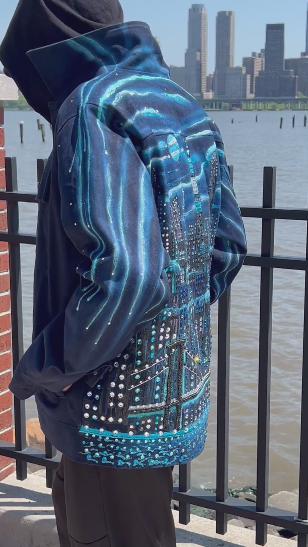 Blue jacket with Loria NYC Art on the back with the city skyline in the background.
