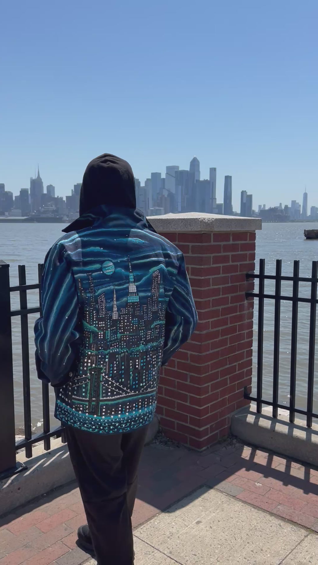 Person wearing a jacket with Loria NYC Art on the back with the city skyline in the background.