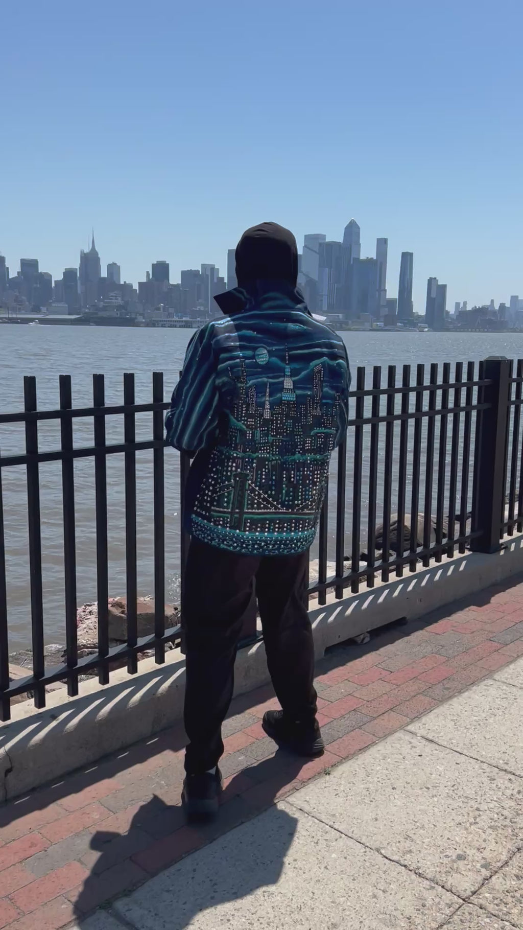 Blue colorful jacket with Loria NYC Art on the back with the city skyline in the background.