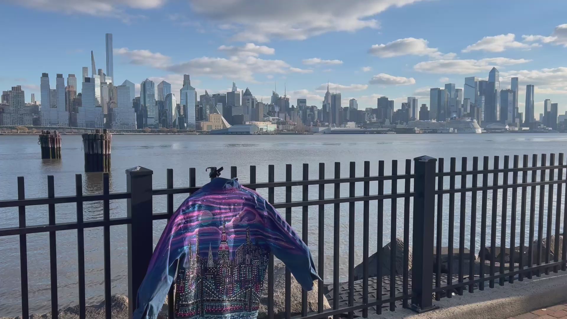 Video on a bright day with a colorful Loria NYC Art jacket and the city skyline in the background 
