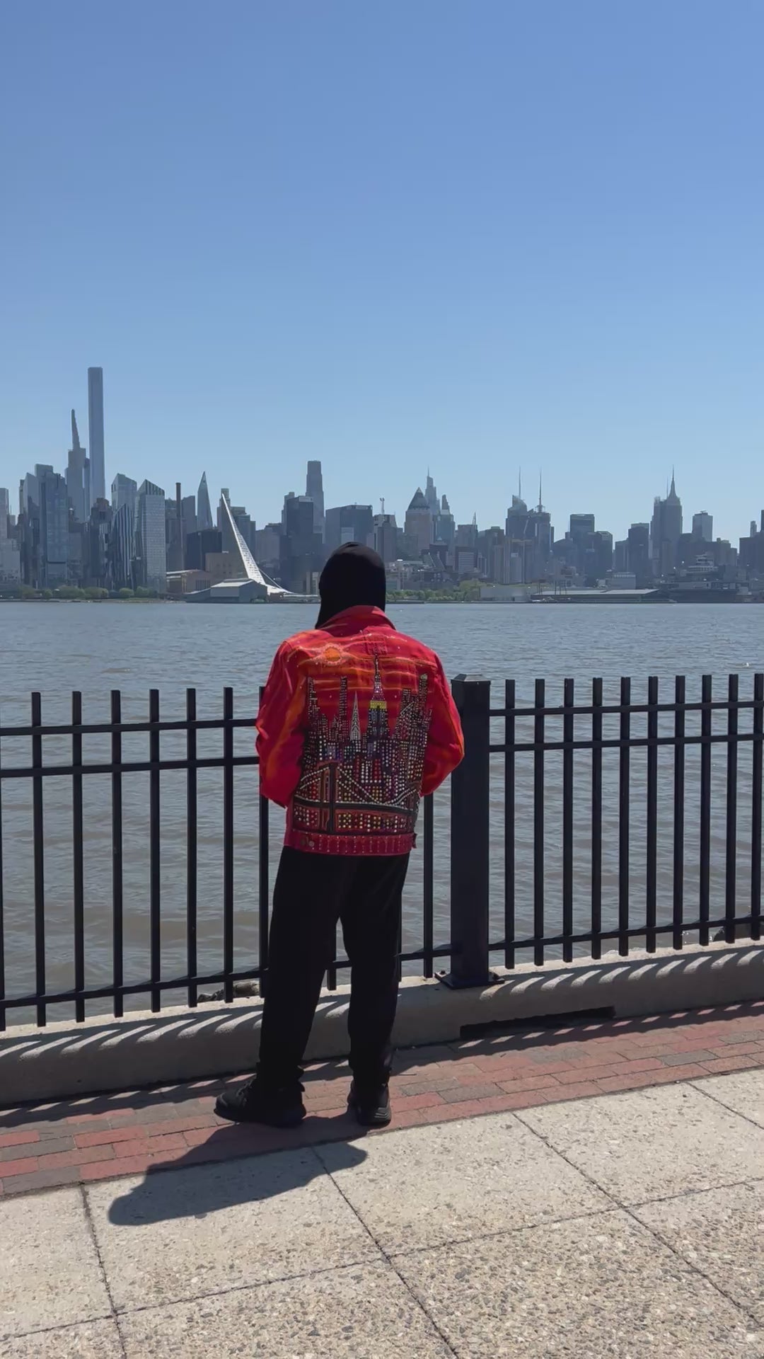 Man in video wearing an orange Loria NYC Art jacket walking in front of the city skyline