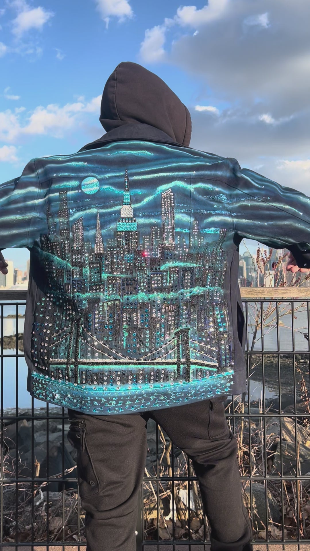 Video of man  on a clear day wearing a  jacket covered in Loria NYC Art with skyline background