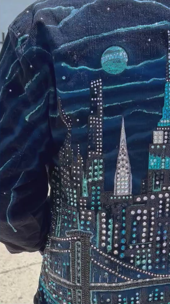 Man wearing a blue jacket with Loria NYC Art on back walking in a video