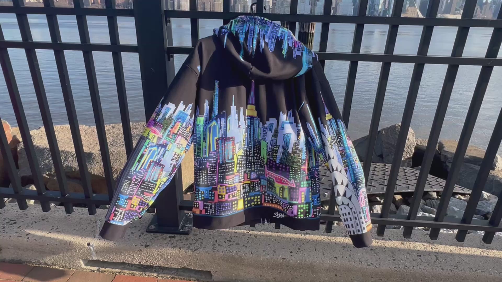Video clip on Loria NYC Art hoodie hanging on a handrail with the NYC skyline in the background 