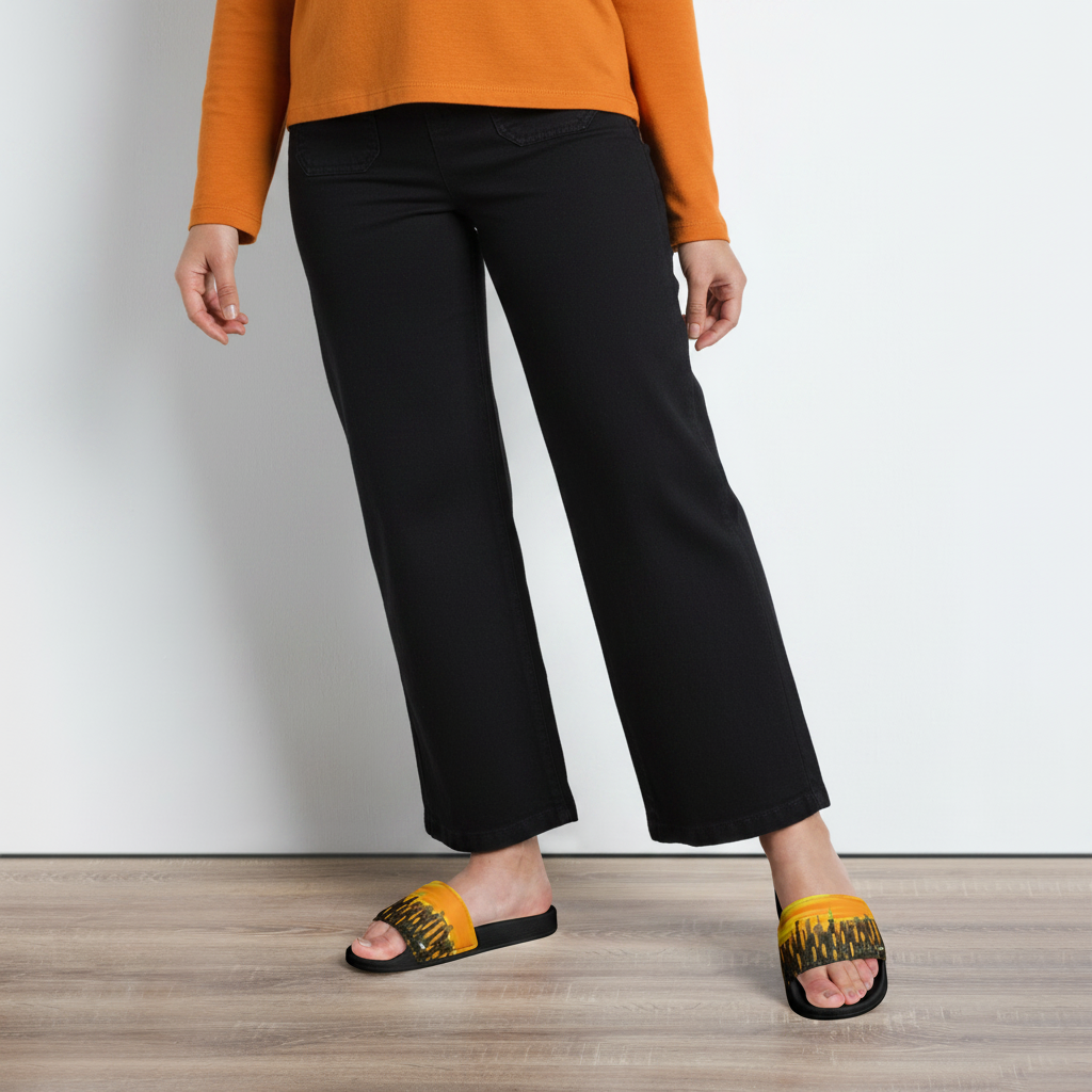 Person wearing white pants and floral Loria NYC Art sandals on a wooden floor.